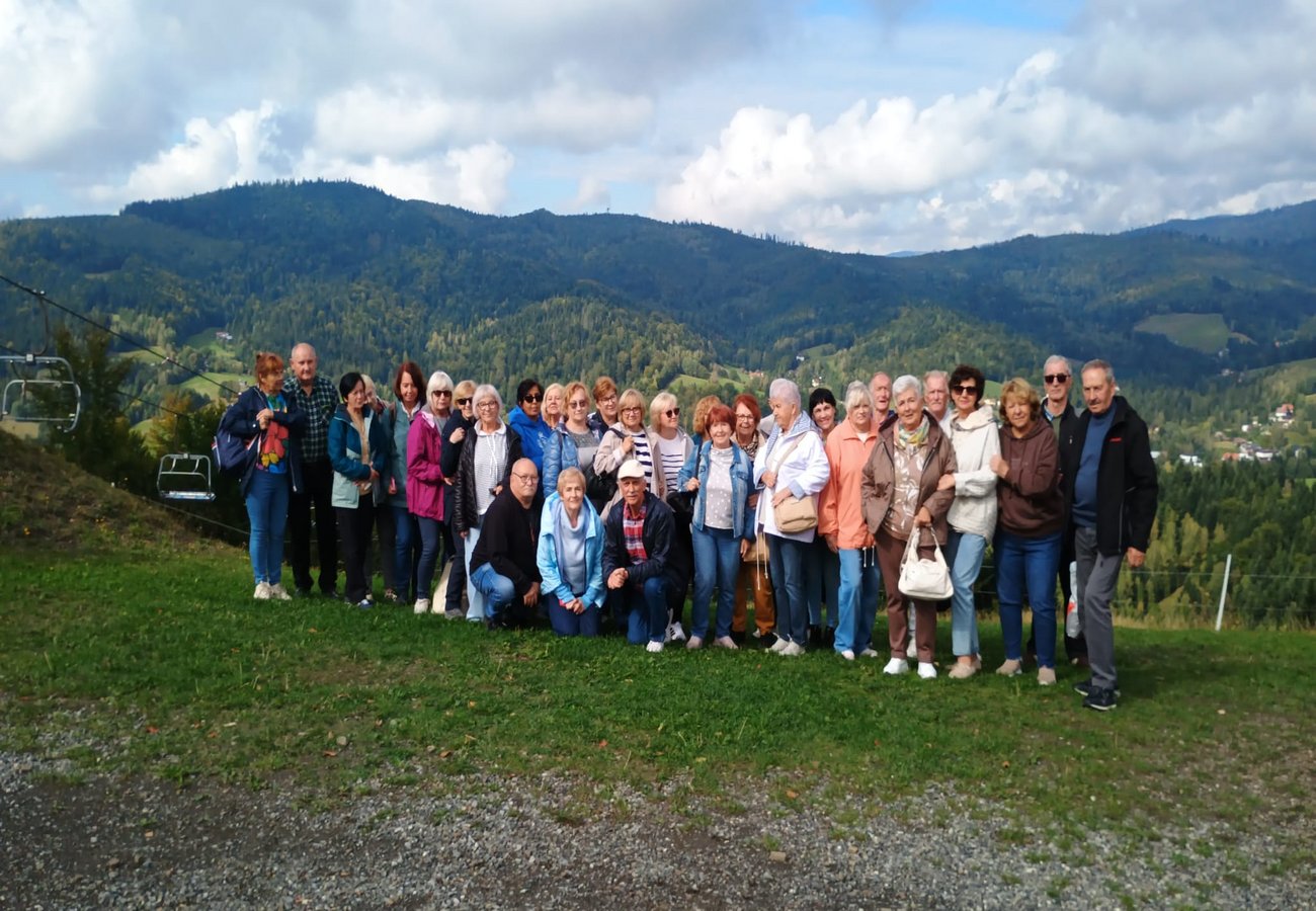 Liczna grupa turystów pozuje do pamiątkowego zdjęcia na zielonym zboczu górskim z panoramą Beskidów w tle
